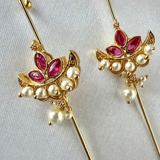 Gold ear pins with red kemp stones and pearls on a light gray background