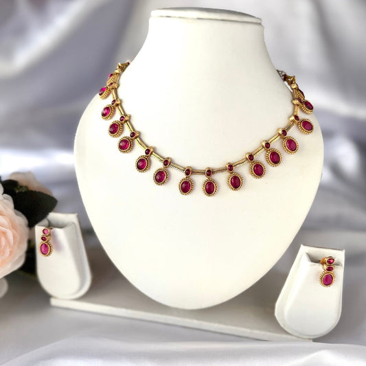 Gold necklace with red gemstones on a white mannequin bust, accompanied by matching earrings.