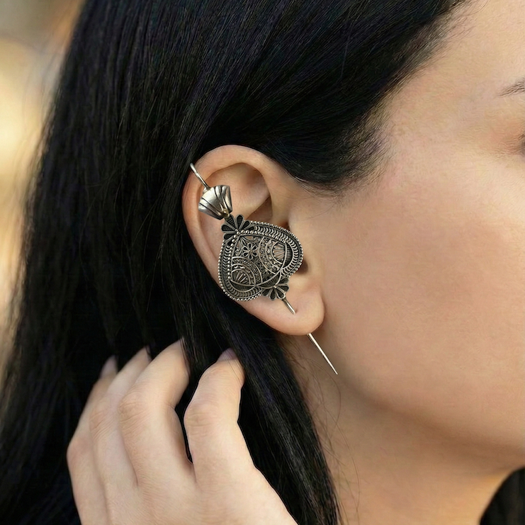 Close-up of a person wearing an ornate silver ear pin with a blurred background