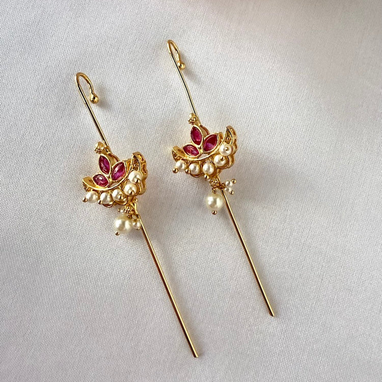 Gold ear pins with red kemp stones and pearl accents on a light gray background