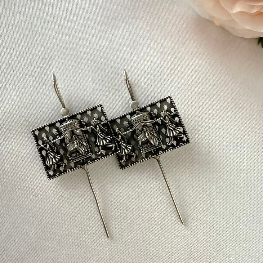 Pair of oxidised ear pins with intricate designs on a light gray background