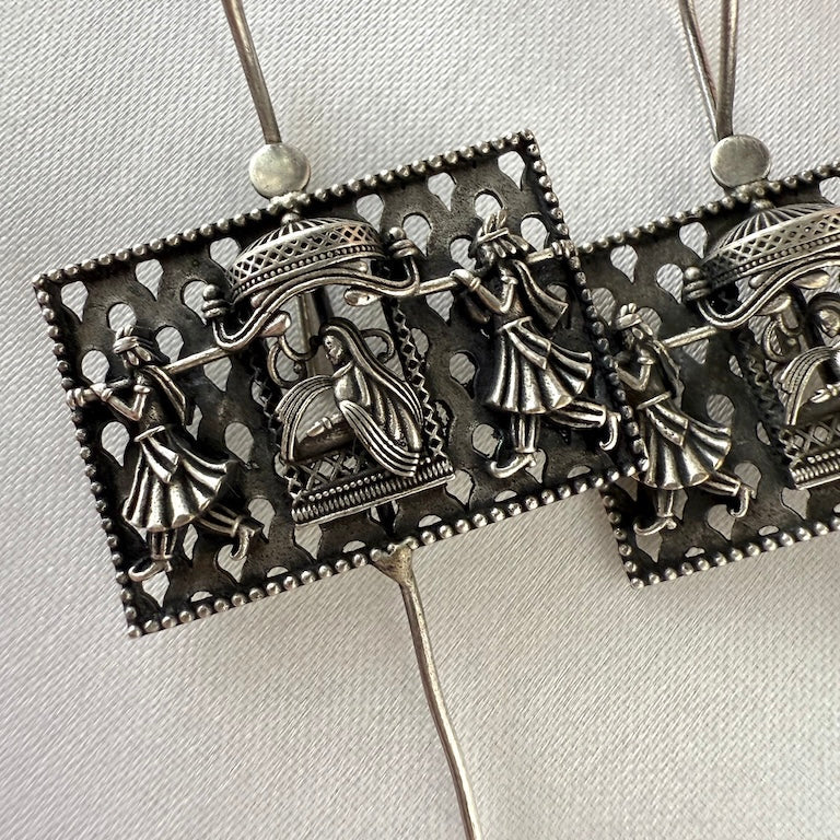 Pair of silver ear pins with intricate designs on a light gray background