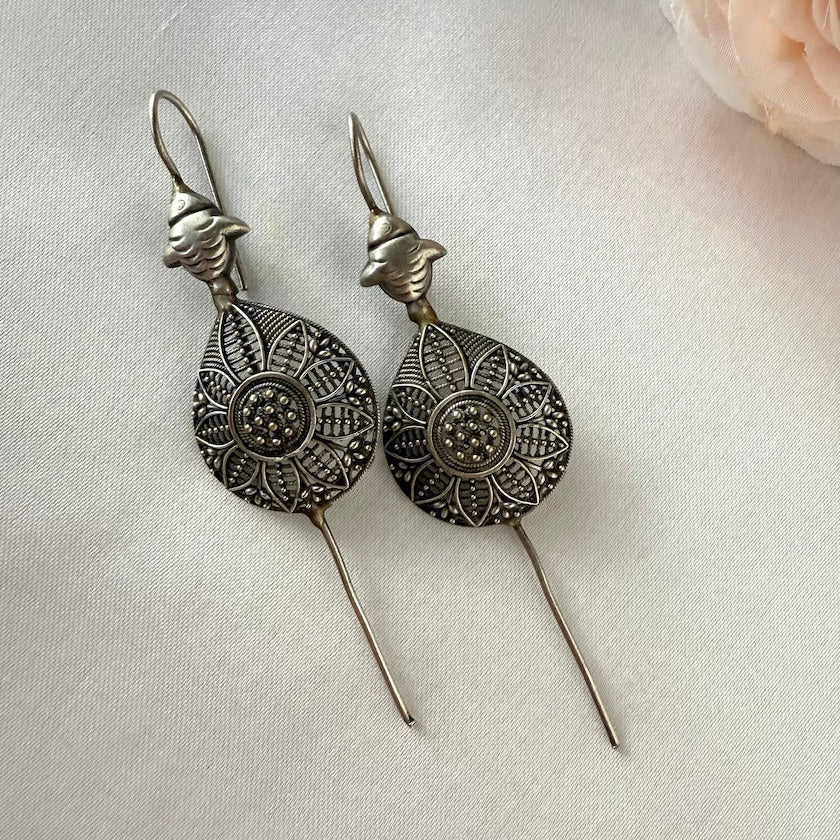 Pair of silver ear pins with intricate designs on a light background