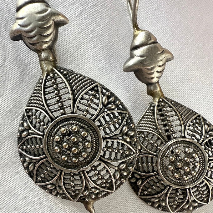 Pair of silver ear pins with intricate designs on a light gray background
