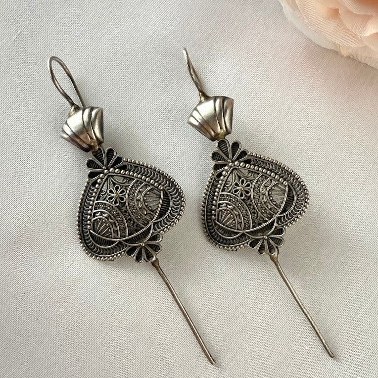 Pair of silver filigree ear pins on a light fabric background with a pink flower.