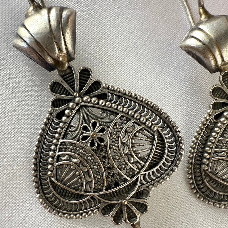 Decorative silver ear pin with intricate designs on a light gray background