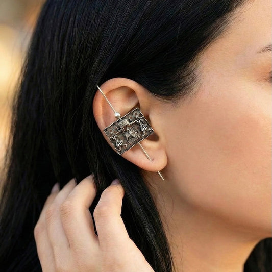 Close-up of a person wearing an ornate ear pin with a blurred background