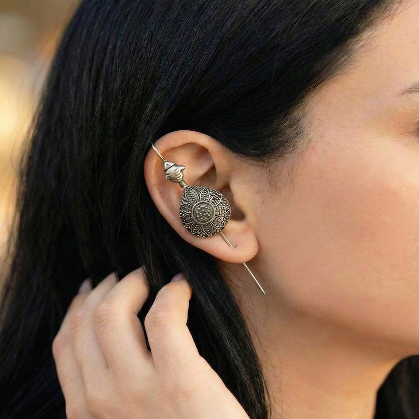 Close-up of a person wearing an ornate ear pin with a blurred background