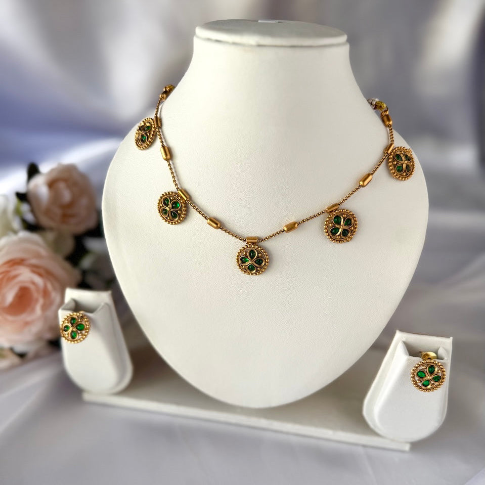 Gold necklace with green gemstones on a white mannequin bust, surrounded by flowers.