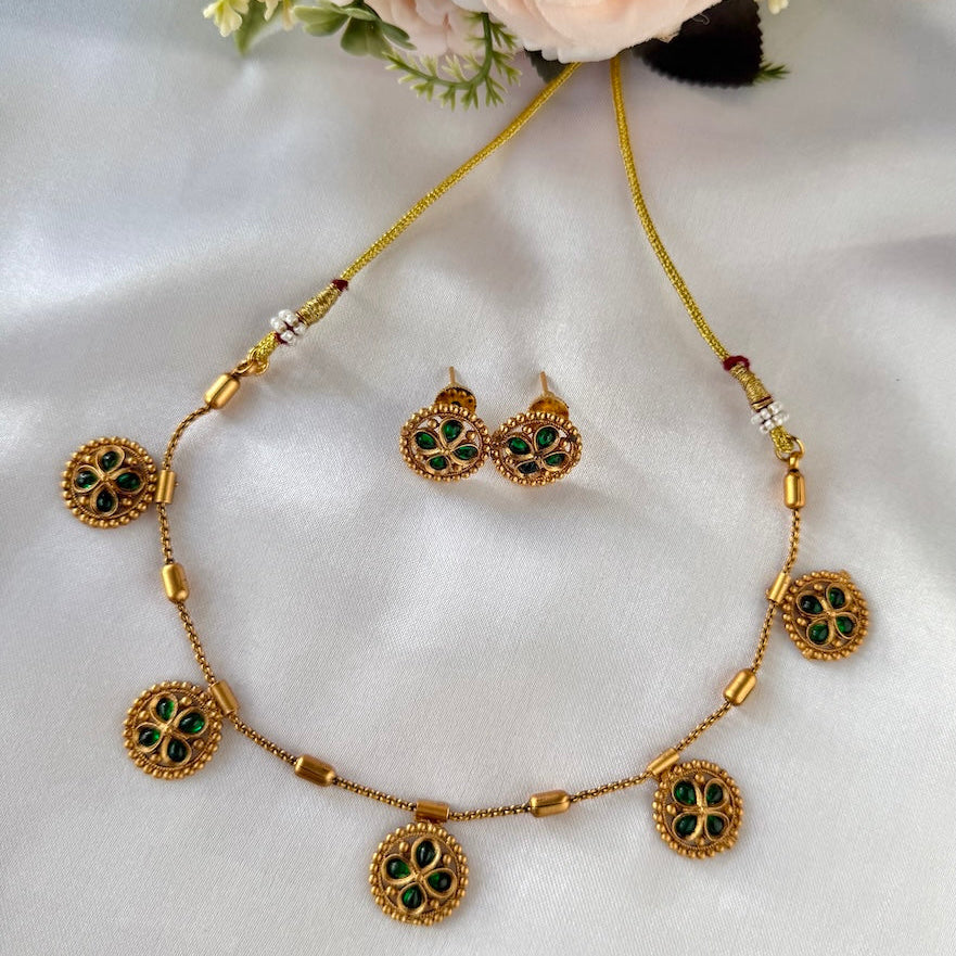 Gold necklace with green gemstones and matching earrings on a white fabric background with flowers.
