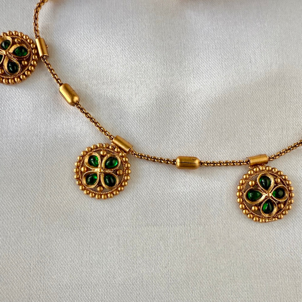 Gold necklace with green gemstones on a white background