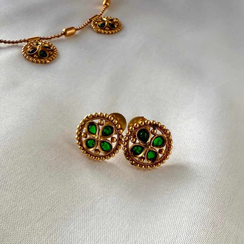 Gold earrings with green gemstones on a white fabric background