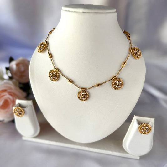 Gold necklace and earrings on a white stand with a blurred floral background