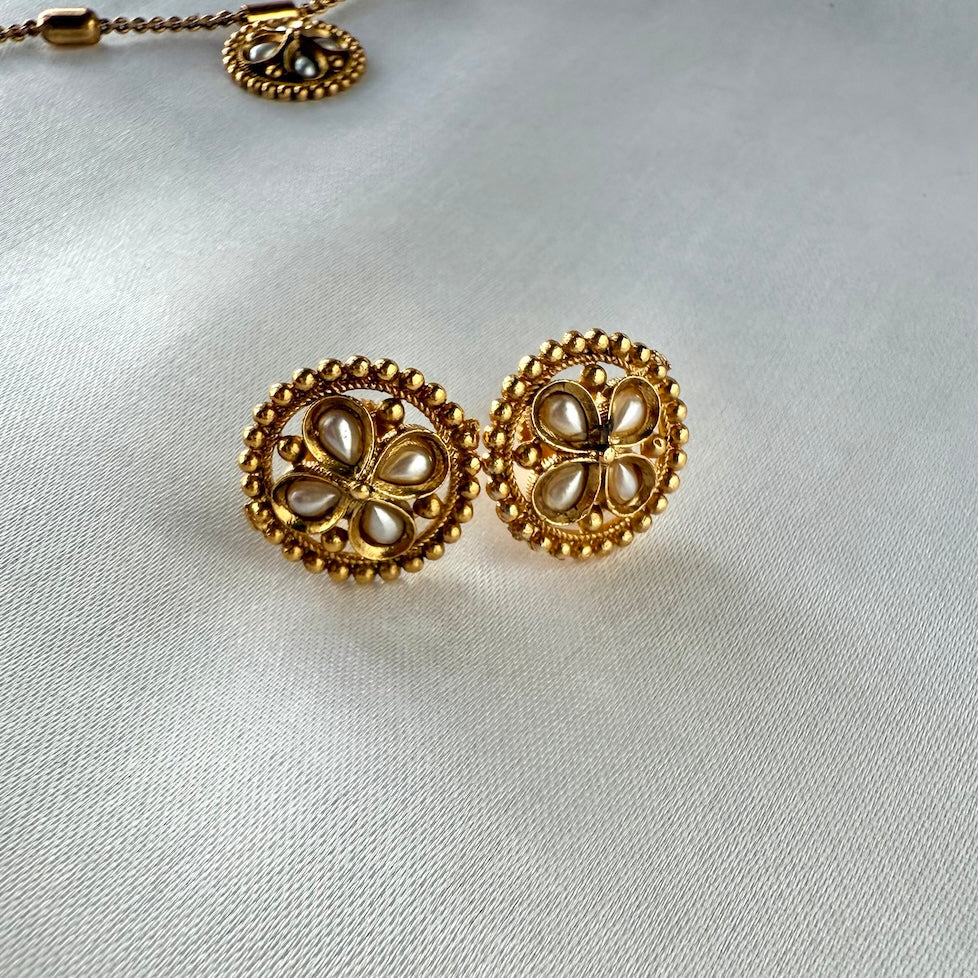 Gold earrings with pearl-like centers on a light gray background