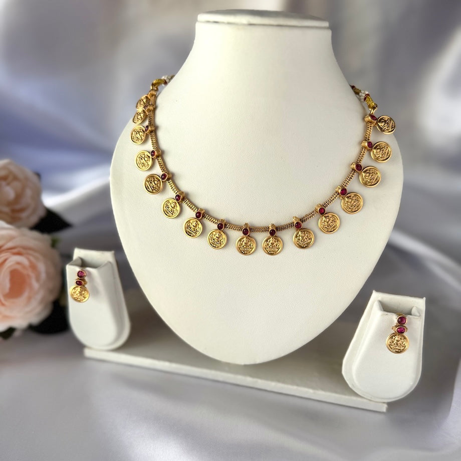 Gold necklace and earrings on a white stand with a soft gray background
