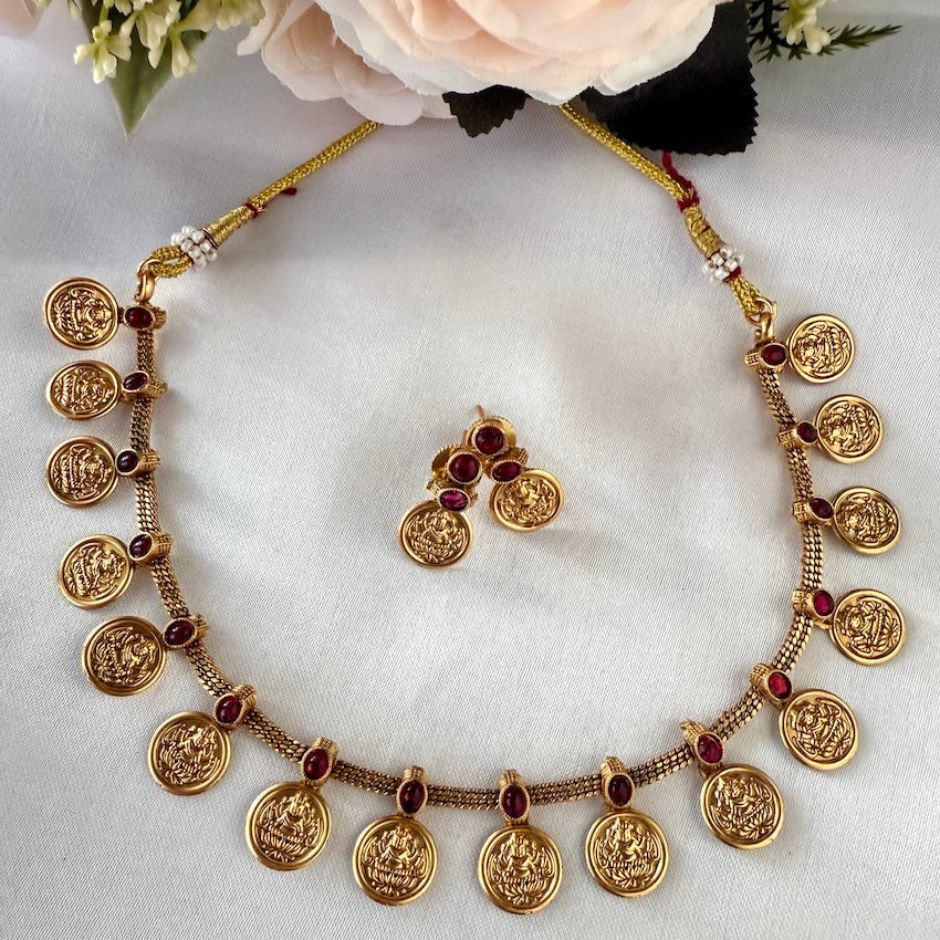 Gold necklace with coin-like pendants and matching earrings on a white background with flowers.