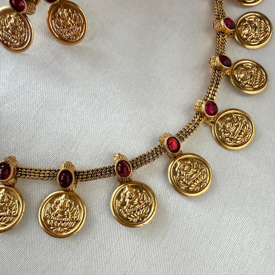 Gold necklace with circular pendants and red stones on a light background