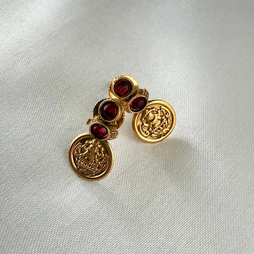 Gold earrings with red gemstones on a light gray fabric background