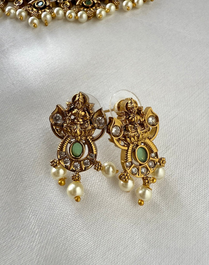 Gold earrings with green stones and pearl drops on a light gray background