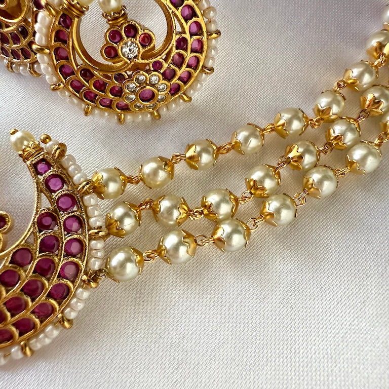 Gold necklace with pearl and red stone detailing on a white background