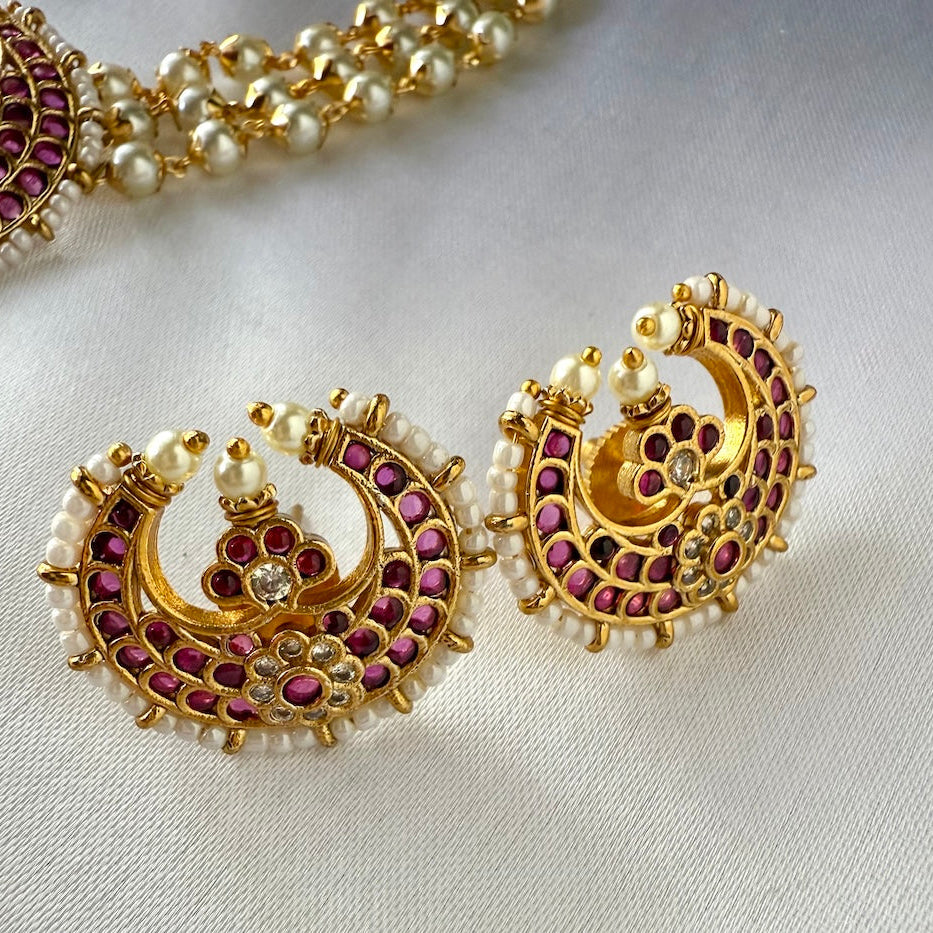 Gold earrings with red stones and pearls on a light background