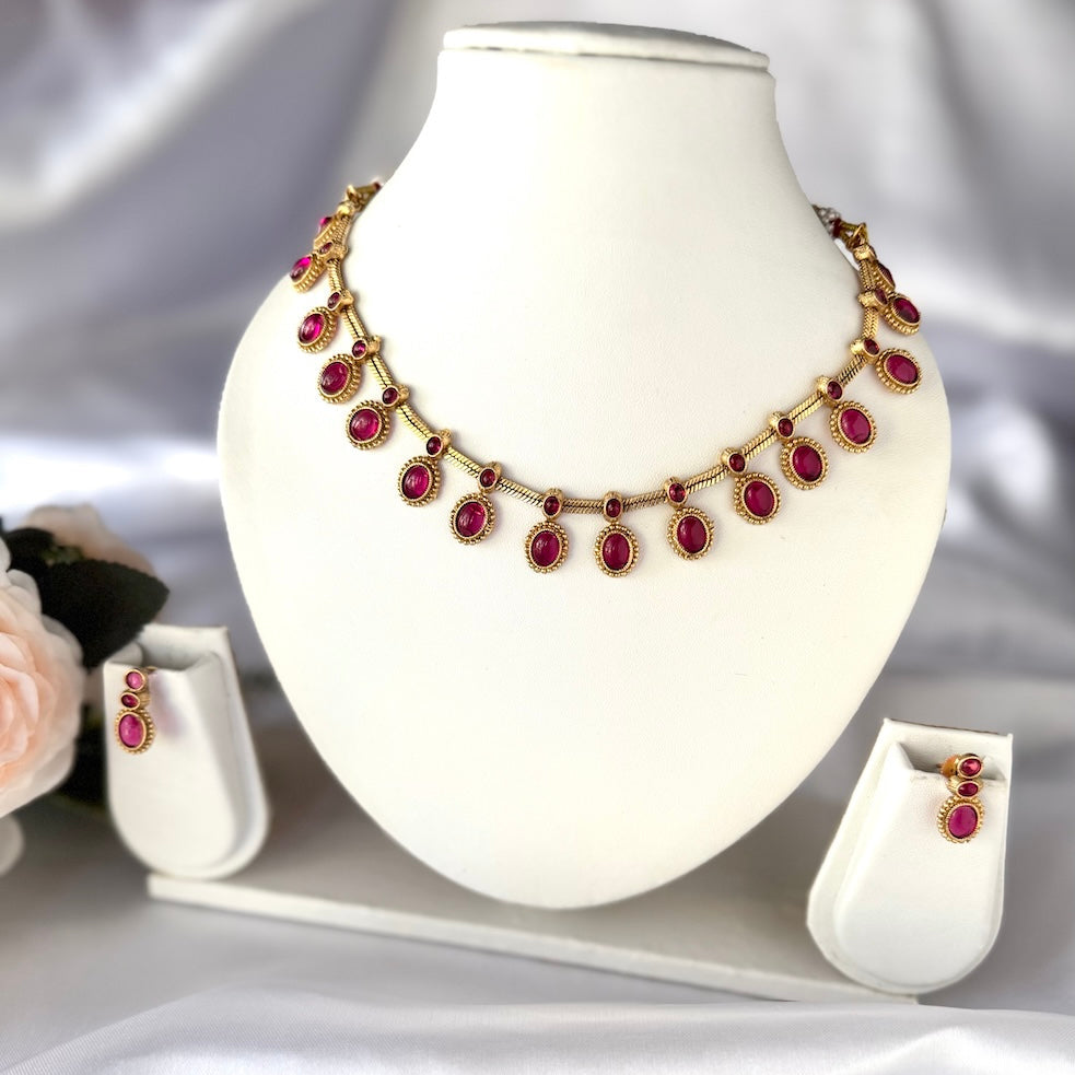 Gold necklace with red gemstones on a white mannequin bust, accompanied by matching earrings.