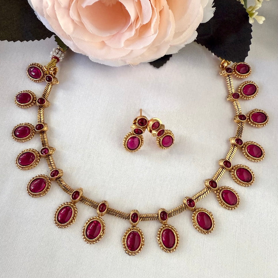 Jewelry set with necklace and earrings featuring red gemstones on a white fabric background.
