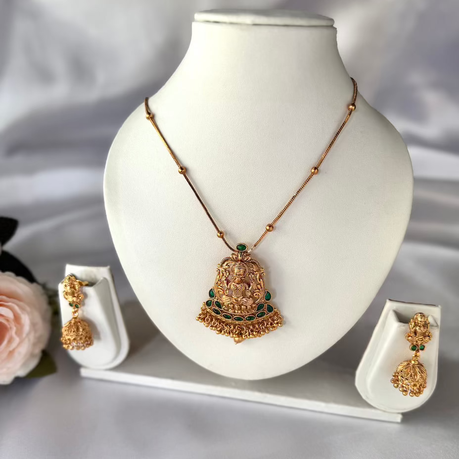 Gold necklace with green gemstones on a white mannequin bust, accompanied by matching earrings.
