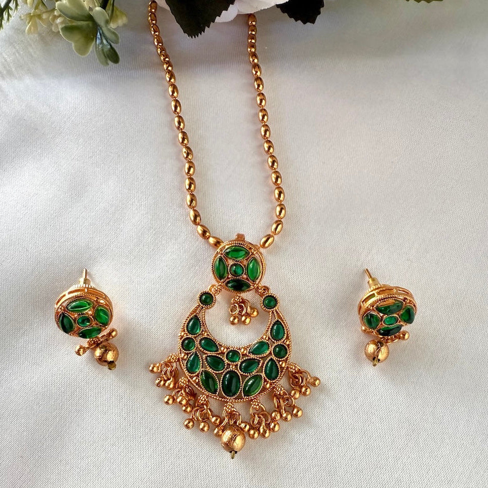 Gold necklace with green gemstones and matching earrings on a white background