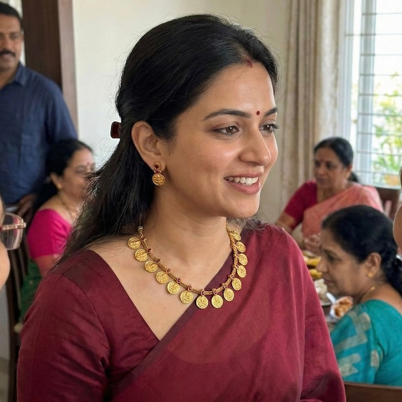 Woman in a maroon saree with gold jewelry in a social setting